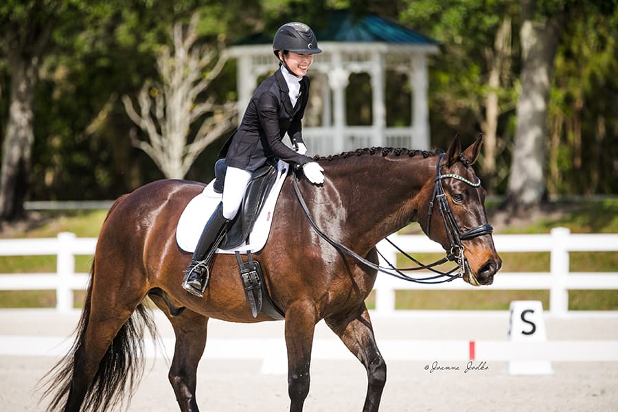 Yuka riding a bay horse along a white arena fence